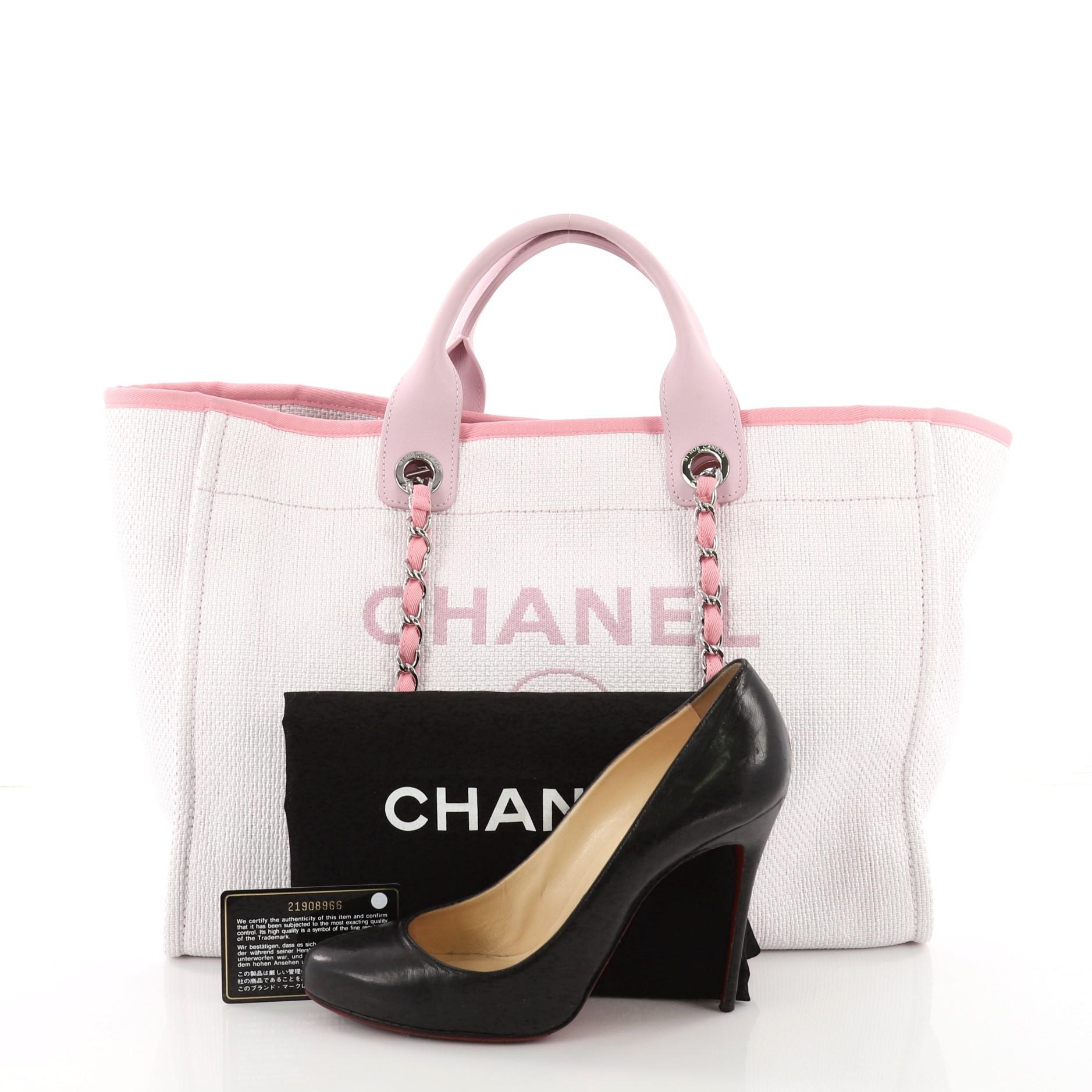 This Chanel Deauville Chain Tote Raffia Large, crafted from white and pink raffia, features dual leather handles, woven-in canvas chain straps, and silver-tone hardware. Its magnetic snap closure opens to a pink fabric interior with slip and zip