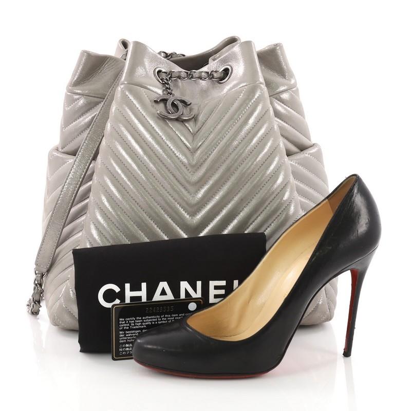 This Chanel Urban Spirit Drawstring Bag Iridescent Chevron Calfskin Large, crafted from grey iridescent chevron calfskin, features a woven-in leather chain strap with leather padding, exterior side slip pockets, and aged silver-tone hardware. Its
