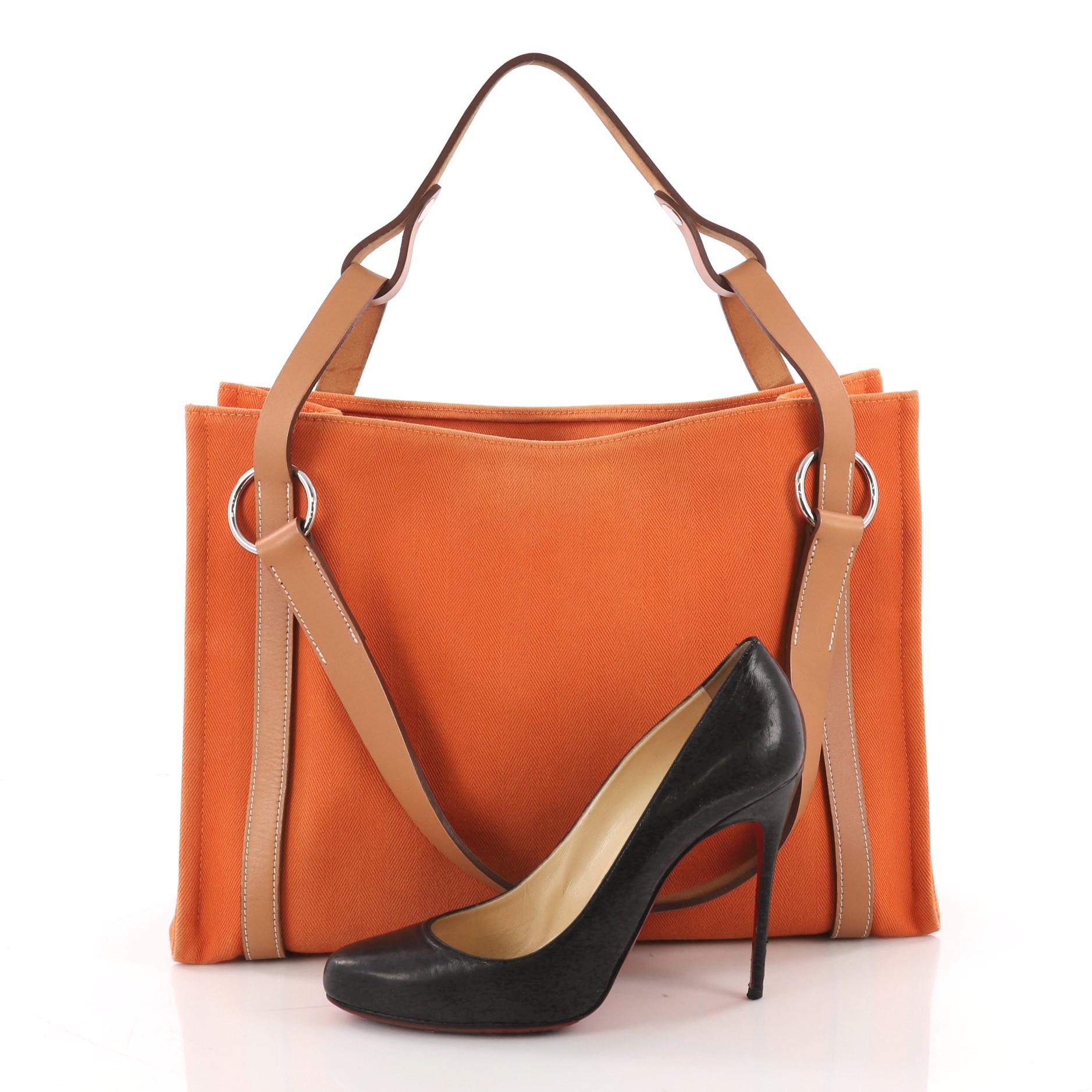 This Hermes Cabalicol Tote Toile with Leather PM, crafted from orange toile fabric, features a leather top handle, brown leather trims, and palladium-tone hardware. Its wide open top showcases an orange toile interior with side slip pockets. Date