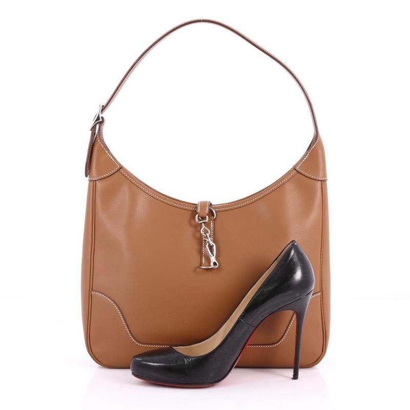 This Hermes Trim II Handbag Epsom 31, crafted from gold epsom leather, features adjustable shoulder strap, palladium tone frontal clasp and palladium-tone hardware. Its zip closure opens to a brown leather interior with zip and slip pockets. Date