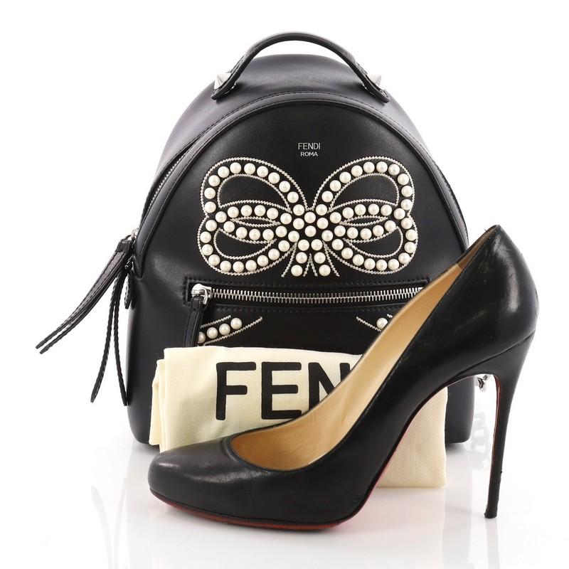 This Fendi Front Zip Backpack Embellished Leather Mini, crafted from embellished black leather, features a flat top-handle with cone-shaped studs, adjustable shoulder straps, exterior front zip pocket, and silver-tone hardware. Its two-way zip
