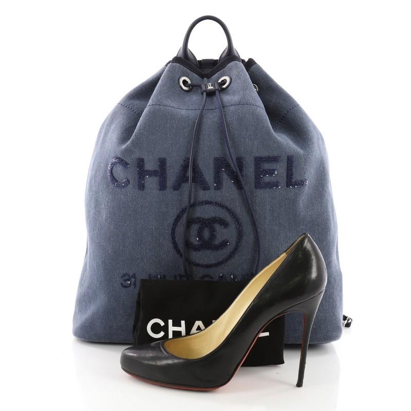 This Chanel Deauville Backpack Canvas with Sequins Large, crafted from blue denim, features a rolled top handle, leather shoulder straps, sequin Chanel logo and store address, and silver-tone hardware. Its drawstring closure opens to a navy blue