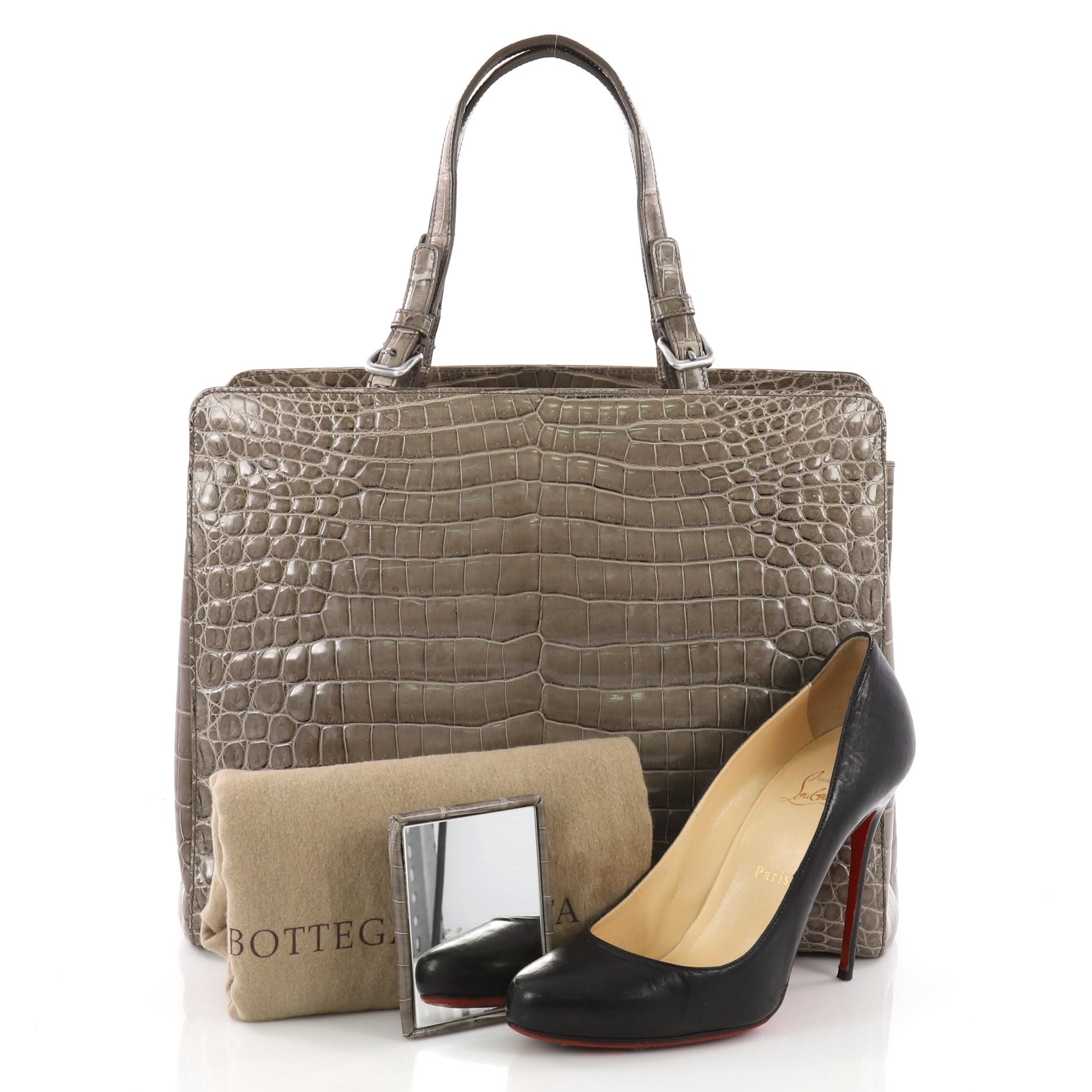 This Bottega Veneta Belted Tote Crocodile Medium. crafted from genuine taupe crocodile, features dual crocodile handles with belt and buckle accents and gunmetal-tone hardware. It opens to a taupe leather interior divided into two compartments with