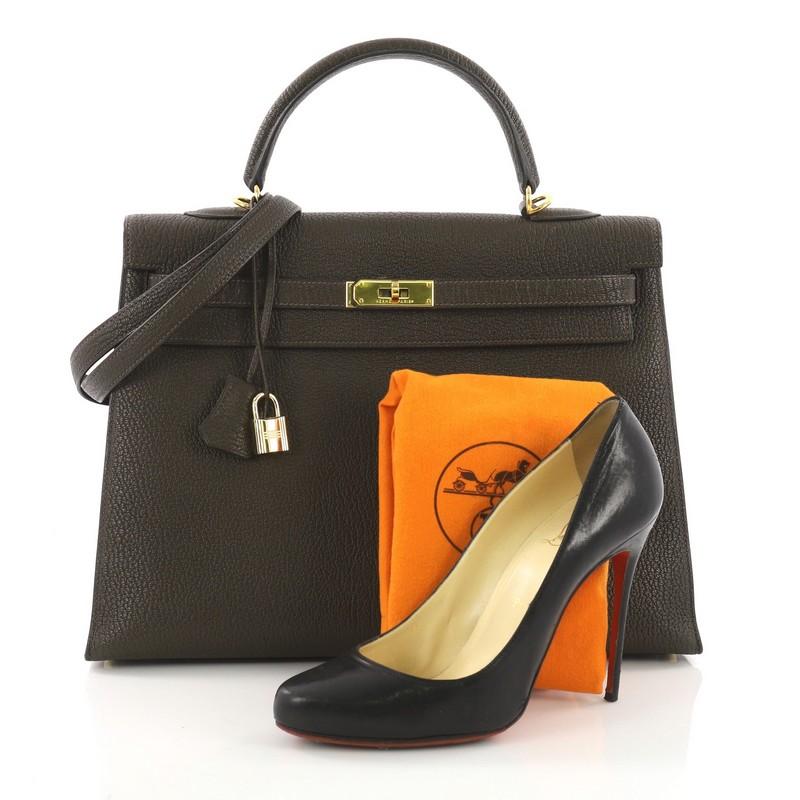 This Hermes Kelly Handbag Vert Olive Chevre Mangalore with Gold Hardware 35, crafted from green Vert Olive Chevre de Coromandel leather, features a single top handle strap, turn-lock closure, and gold-tone hardware. Its turn-lock closure opens to a