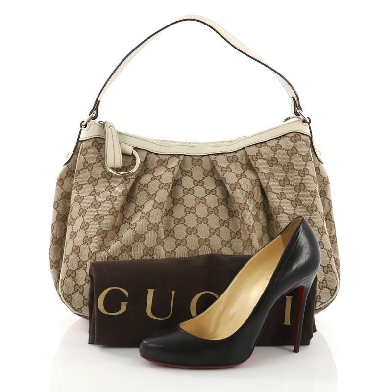 This Gucci Sukey Hobo GG Canvas Medium, crafted from brown GG monogram canvas with off-white leather trims, features a leather strap that sit comfortably on the shoulders, a ruched silhouette, and gold tone hardware. Its top zip closure opens to a