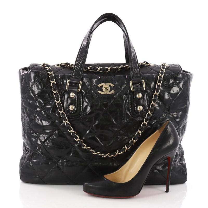 This Chanel Portobello Tote Quilted Glazed Calfskin Large, crafted from black quilted glazed calfskin, features dual flat leather handles, woven-in leather chain straps, and gold-tone hardware. Its turn-lock closure opens to a gray fabric interior