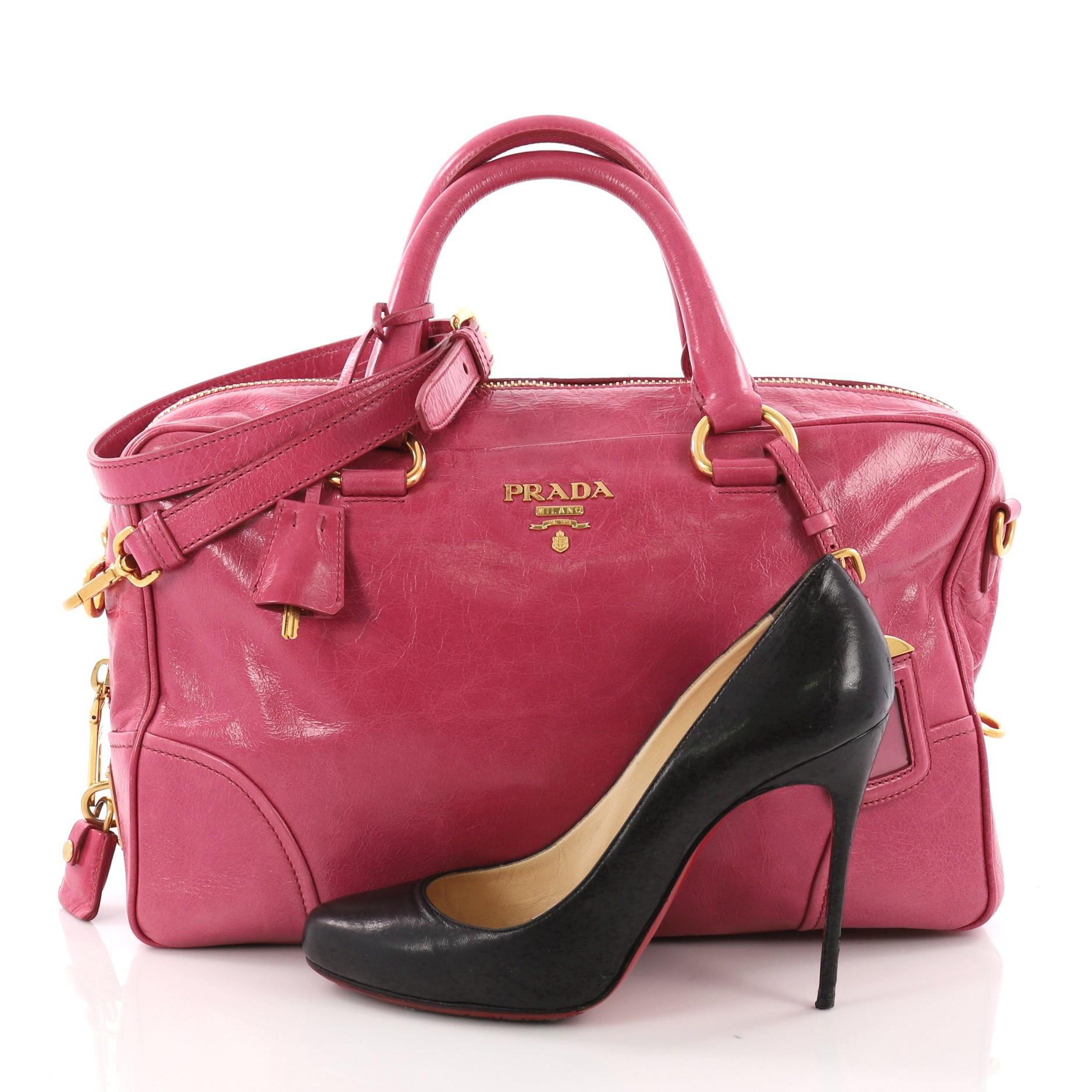 This Prada Convertible Bauletto Bag Vitello Shine Medium, crafted in pink vitello shine leather, features dual rolled leather handles, protective base studs, and gold-tone hardware. Its zip closure opens to a pink fabric interior with zip and slip