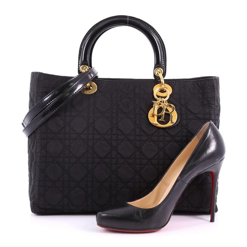 This Christian Dior Lady Dior Handbag Cannage Quilt Nylon Large, crafted in black cannage quilt nylon, features short dual handles with sleek Dior charms and gold-tone hardware. Its top zip closure opens to a red fabric interior with a zip pocket.