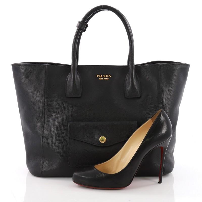 This Prada Front Pocket Convertible Tote Saffiano Leather, crafted from black saffiano leather, features dual rolled top handles, exterior front snap pockets, and gold-tone hardware. Its snap button closure opens to a gray leather interior with side