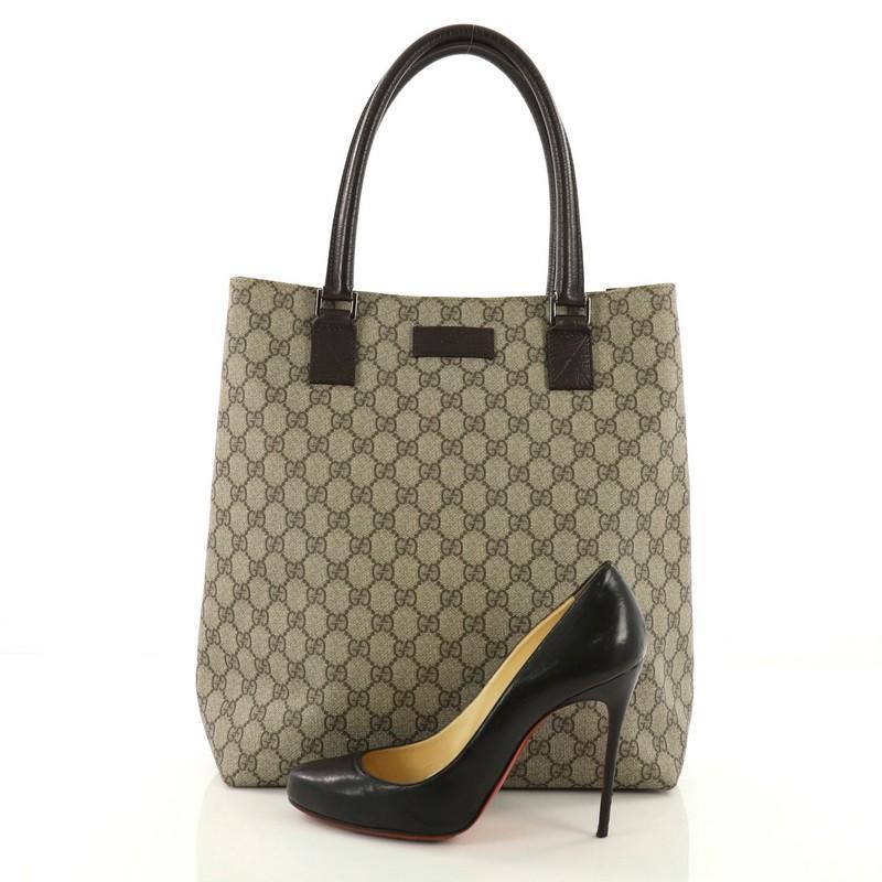 This Gucci Open Tote GG Coated Canvas Tall, crafted from brown GG coated canvas, features dual top handles, brand logo at its center, and silver-tone hardware. Its magnetic snap button closure opens to a brown fabric interior with side zip and slip