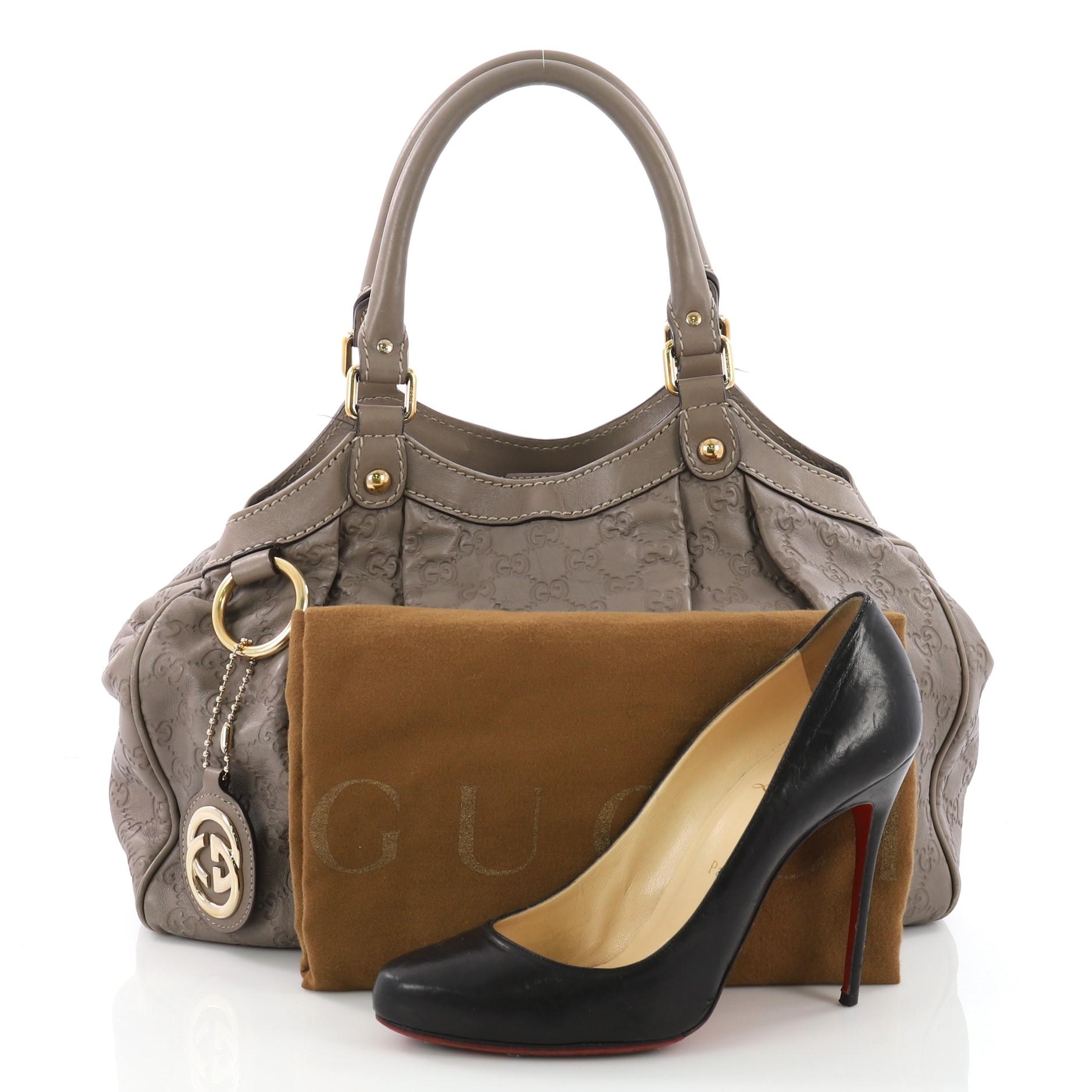 This Gucci Sukey Tote Guccissima Leather Medium, crafted from taupe guccissima leather, dual-rolled leather top handles, side snap buttons, and gold-tone hardware accents. Its top magnetic snap closure opens to a black fabric interior with a side
