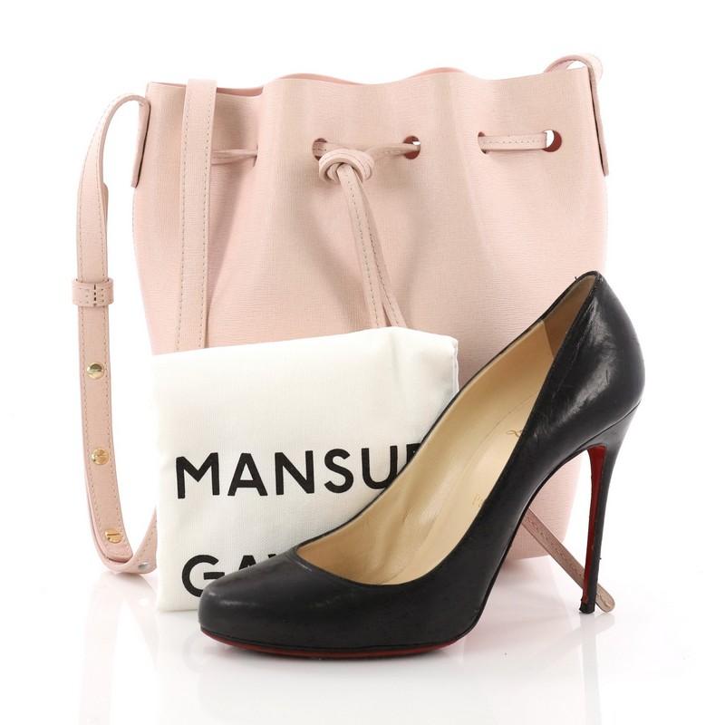 This Mansur Gavriel Bucket Bag Leather Mini, crafted in pink leather, features an adjustable leather shoulder strap, and gold-tone hardware. Its drawstring closure opens to a pink leather interior. **Note: Shoe photographed is used as a sizing