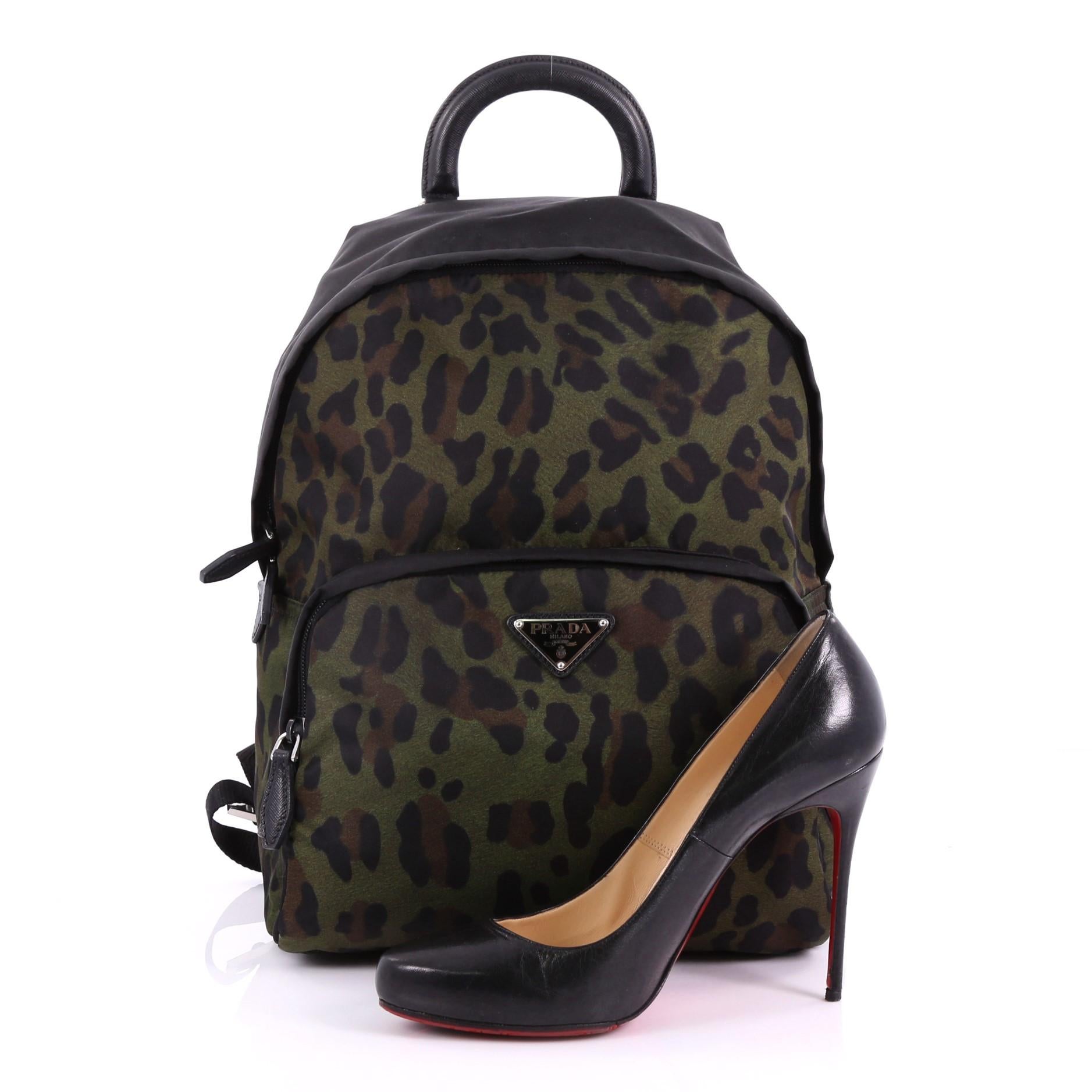 This Prada Front Pocket Backpack Printed Tessuto Medium, crafted in black and green printed tessuto, features a top carry handle, adjustable back shoulder straps, exterior front zip pocket, and silver-tone hardware. Its zip closure opens to a black