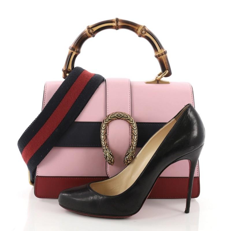 This Gucci Dionysus Bamboo Top Handle Bag Colorblock Leather Medium, crafted from pink colorblock leather, features bamboo top handle, textured tiger head spur detail on its flap, and aged bronze and bamboo hardware. Its closure with side release