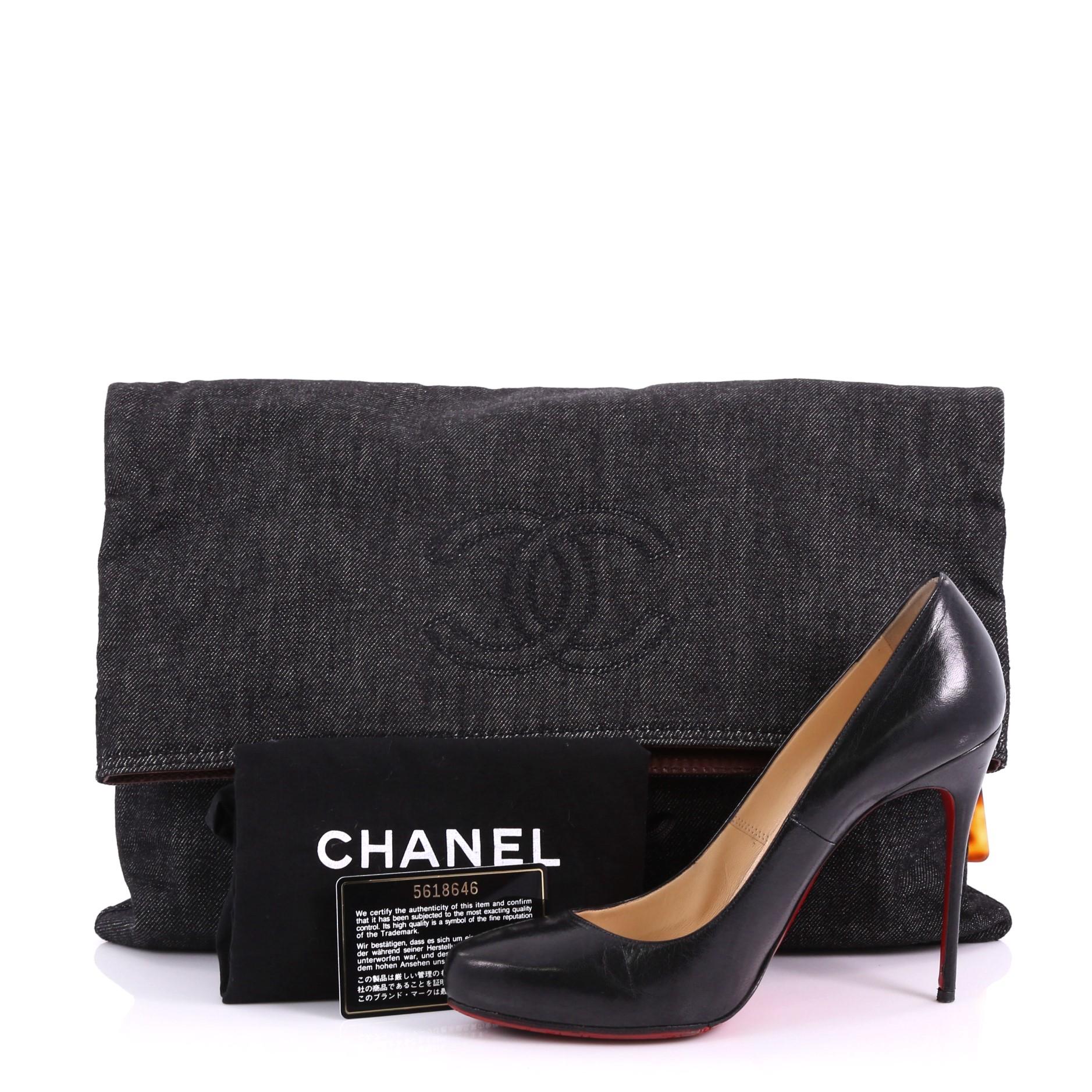 This Chanel Vintage CC Fold Over Clutch Denim Large, crafted from navy denim, features stitched CC logo, fold-over flap, and matte gold-tone hardware. Its magnetic snap button closure opens to a brown fabric interior with zip pocket. Hologram
