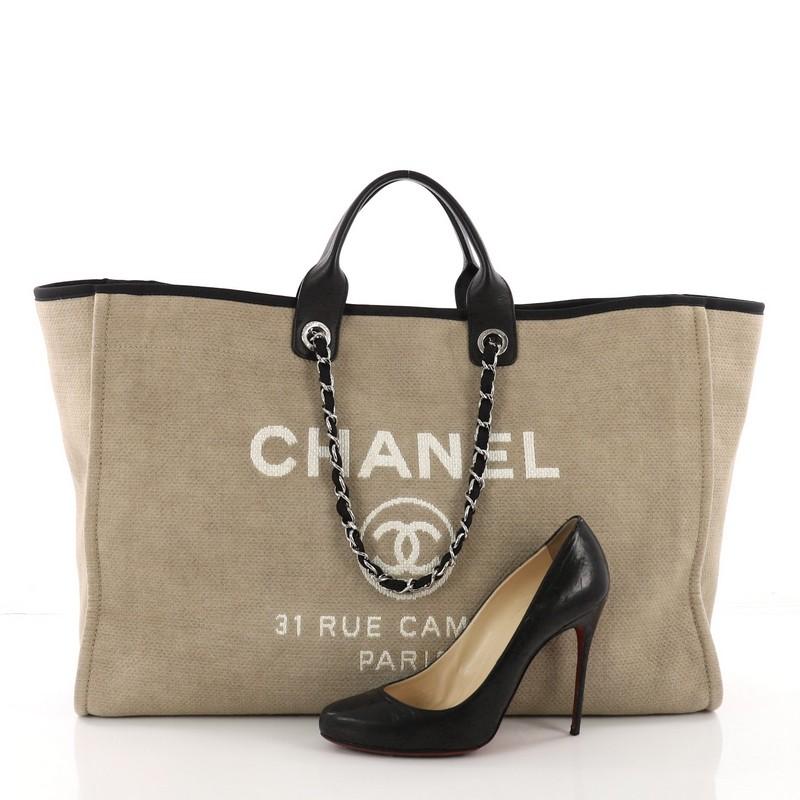 This Chanel Deauville Chain Tote Canvas XL, crafted in beige canvas, features dual-flat leather handles, woven-in chain link straps, embroidered CC logo with Chanel's famous Parisian store address and silver-tone hardware. Its magnetic snap closure