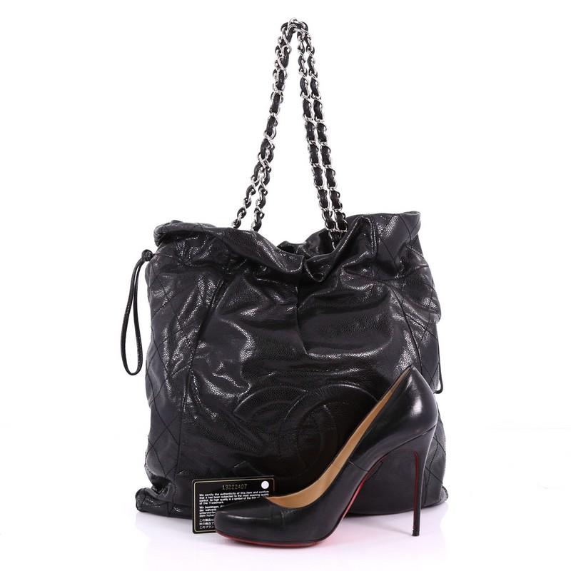 This Chanel Caviar 31 Drawstring Tote Caviar Large, crafted from black caviar leather, features dual woven-in leather chain strap, stitched CC logo at front and silver-tone hardware. ts drawstring closure opens to a black fabric interior with zip