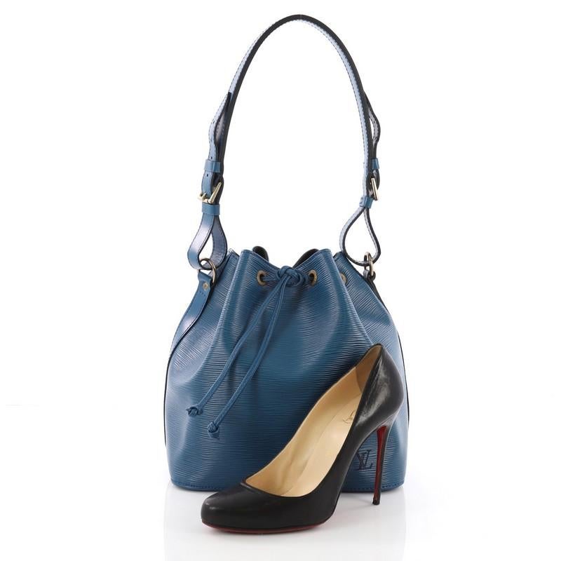 This Louis Vuitton Petit Noe Handbag Epi Leather, crafted from blue epi leather, features adjustable shoulder straps, subtle LV logo, leather drawstring threaded through metal eyelets, and aged gold-tone hardware. Its drawstring closure opens to a