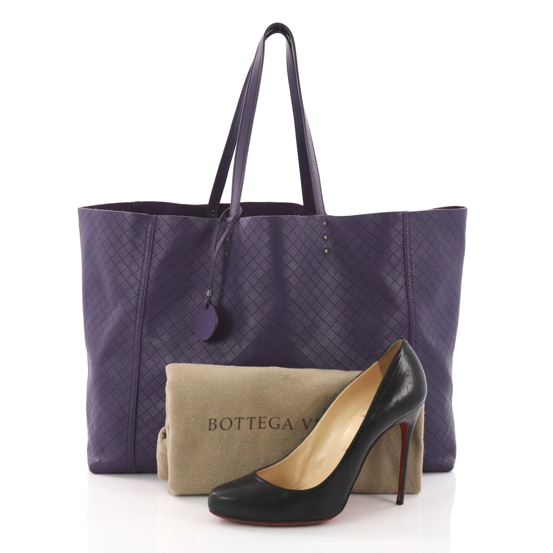 This Bottega Veneta Intrecciomirage Tote Leather Large, crafted in purple intrecciomirage leather, features dual tall leather top handles and gunmetal-tone hardware. It opens to a purple raw leather interior. **Note: Shoe photographed is used as a