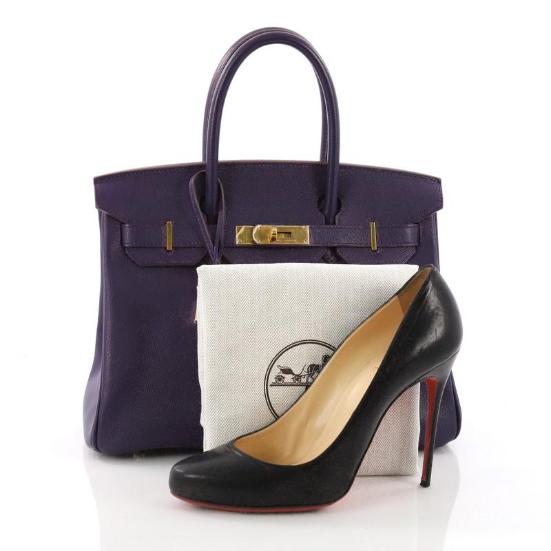 This Hermes Birkin Handbag Iris Epsom with Gold Hardware 30, crafted in Iris epsom leather, features dual rolled top handles, frontal flap, turn-lock closure, and gold-tone hardware. Its turn-lock closure opens to a purple leather interior with slip