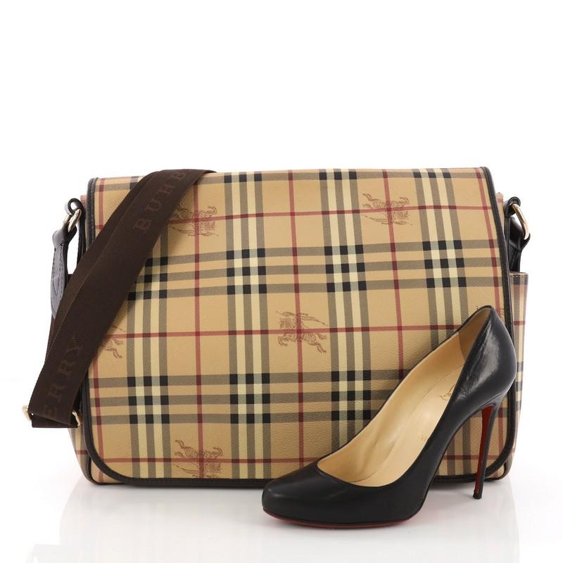 This Burberry Diaper Bag Haymarket Coated Canvas Large, crafted from Haymarket coated canvas, features a long and adjustable canvas shoulder strap, two exterior side pockets, and gold-tone hardware. Its magnetic snap closure opens to a brown fabric