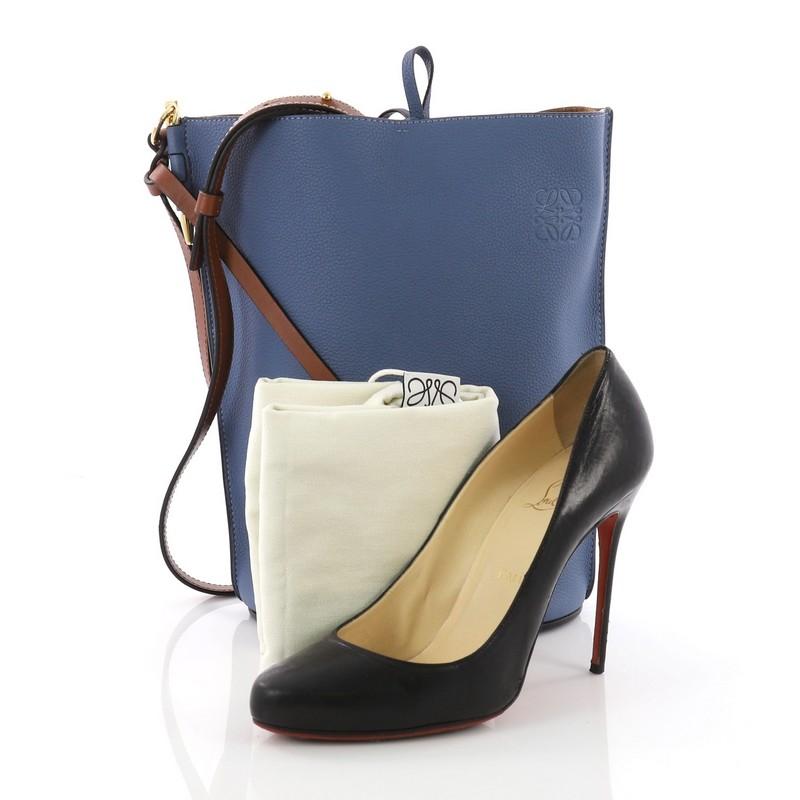 This Loewe Gate Bucket Bag Leather Medium, crafted in blue leather, features an adjustable leather strap, and gold-tone hardware. Its tie closure opens to a brown suede with slip pockets. **Note: Shoe photographed is used as a sizing reference, and