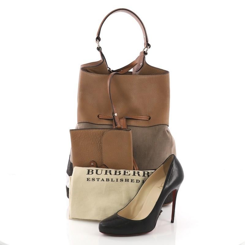 This Burberry Ashby Drawstring Handbag House Check Canvas with Leather Large, crafted in brown house check canvas and leather, features a leather handle and dark gold-tone hardware. Its drawstring closure opens to a black fabric interior. **Note: