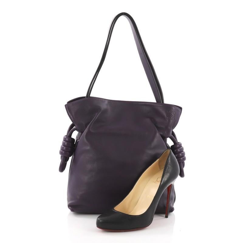 This Loewe Flamenco Knot Bag Leather Small, crafted in purple leather, features leather shoulder strap, drawstring top with oversized tassels, and silver-tone hardware. Its drawstring closure opens to an off-white fabric interior with side zip