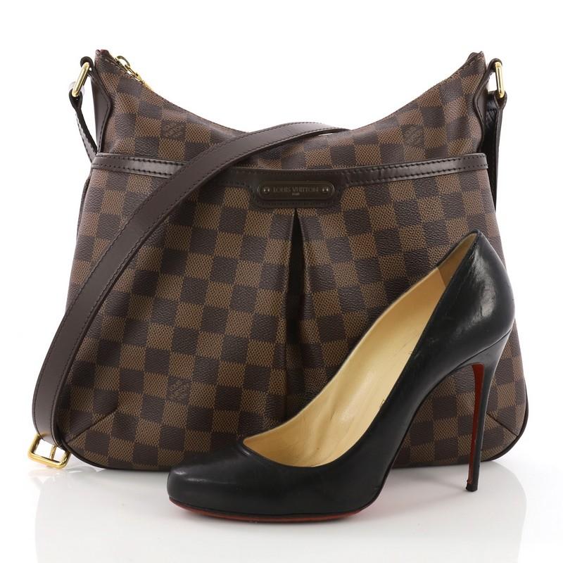 This Louis Vuitton Bloomsbury Handbag Damier PM, crafted in damier ebene coated canvas, features adjustable shoulder strap, exterior front pocket with snap closure, and gold-tone hardware. Its zip closure opens to a red fabric interior with slip