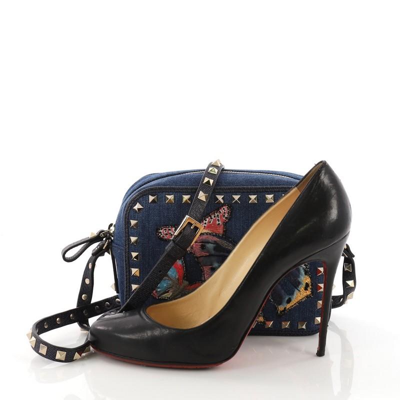 This Valentino Rockstud Camera Crossbody Bag Denim with Butterfly Applique, crafted in blue denim, features butterfly applique, multiple studs, adjustable leather strap with studs and silver-tone hardware. Its zip closure opens to a blue denim