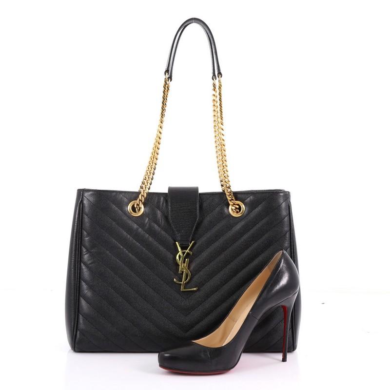 This Saint Laurent Classic Monogram Shopper Matelasse Chevron Leather Large, crafted from black matelasse chevron leather, features dual grommet chain straps with leather pads, distinct YSL logo at the front, and gold-tone hardware. It opens to a