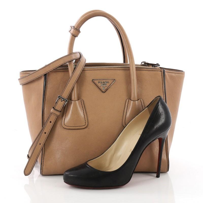 This Prada Twin Pocket Tote Glace Calf Small, crafted in tan glace calf leather, features tall dual rolled top handles, protective base studs and silver-tone hardware. Its top snap closure opens to a black fabric interior with zip and slip pockets.