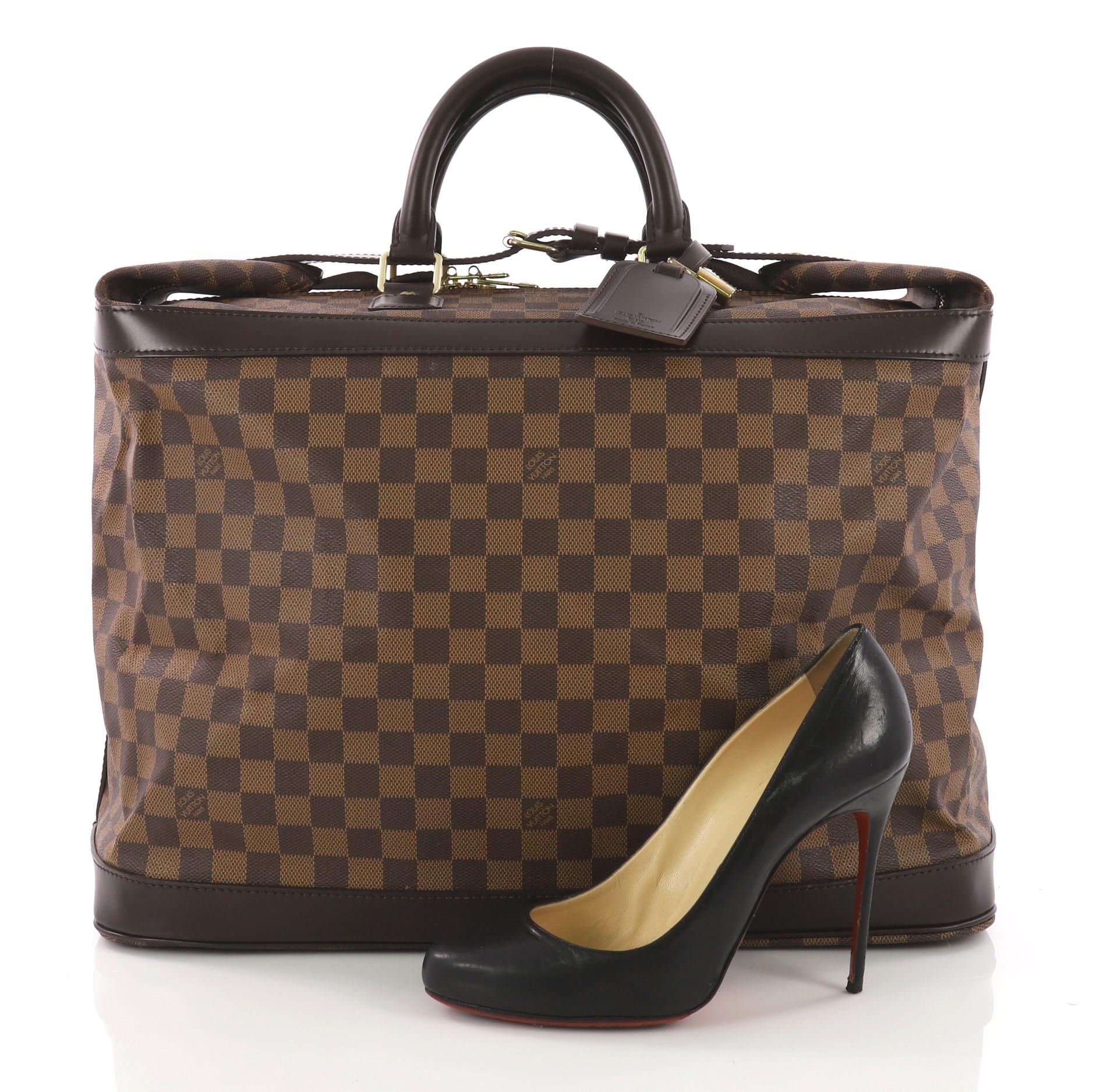 This Louis Vuitton Cruiser Handbag Damier 45, crafted in Louis Vuitton's iconic damier ebene coated canvas, features dual rolled handles, dark brown leather trims, and gold-tone hardware. Its top buckle belt strap and zip closure holds the folded