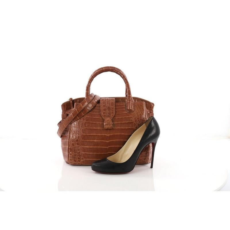 This Nancy Gonzalez Cristina Tote Crocodile Small, crafted from brown genuine crocodile skin, features dual rolled top handles, side gussets with belt detail, and gold-tone hardware. Its top zip closure opens to a brown suede interior divided into