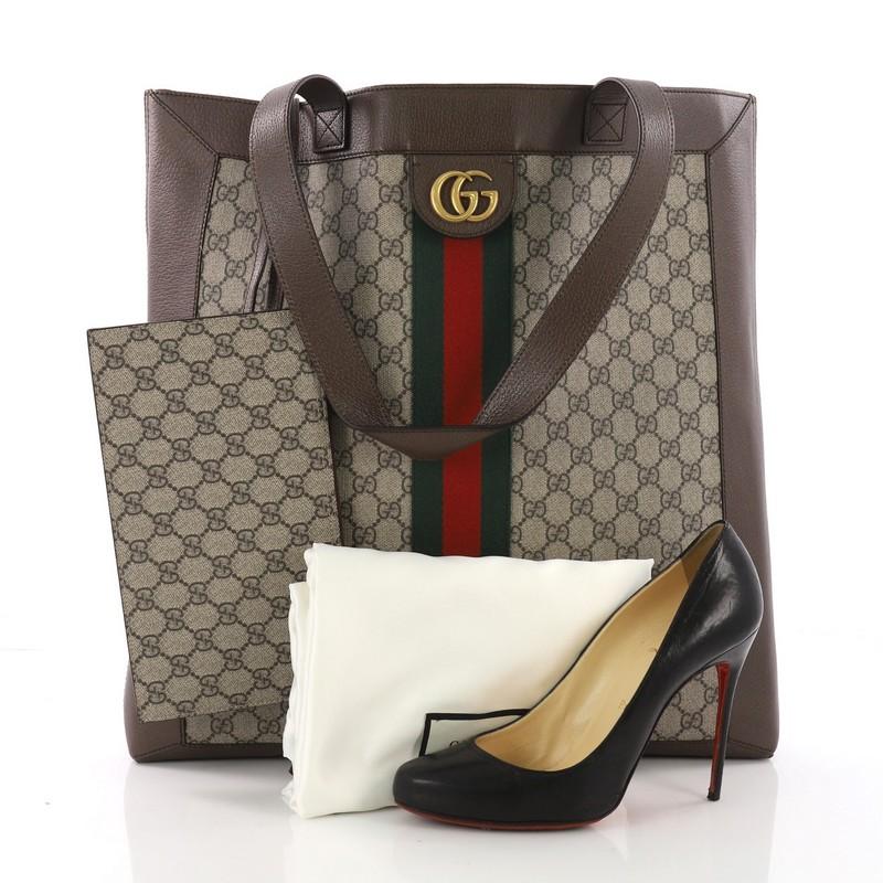 This Gucci Ophidia Soft Open Tote GG Coated Canvas Large, crafted in brown GG coated canvas, features dual leather shoulder strap, Gucci web design, and aged gold-tone hardware. It opens to a beige microfiber interior. **Note: Shoe photographed is