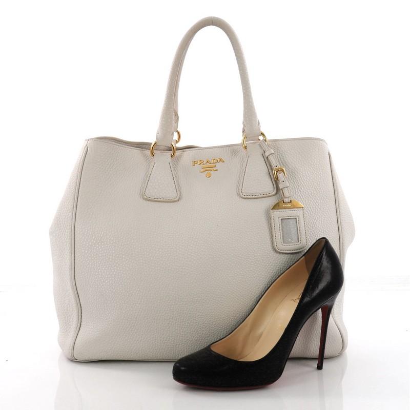 This Prada Convertible Shopper Tote Vitello Daino Large, crafted from off white vitello daino leather, features dual rolled leather handles, side snap buttons, and gold-tone hardware. It opens to a beige fabric interior with side zip and slip