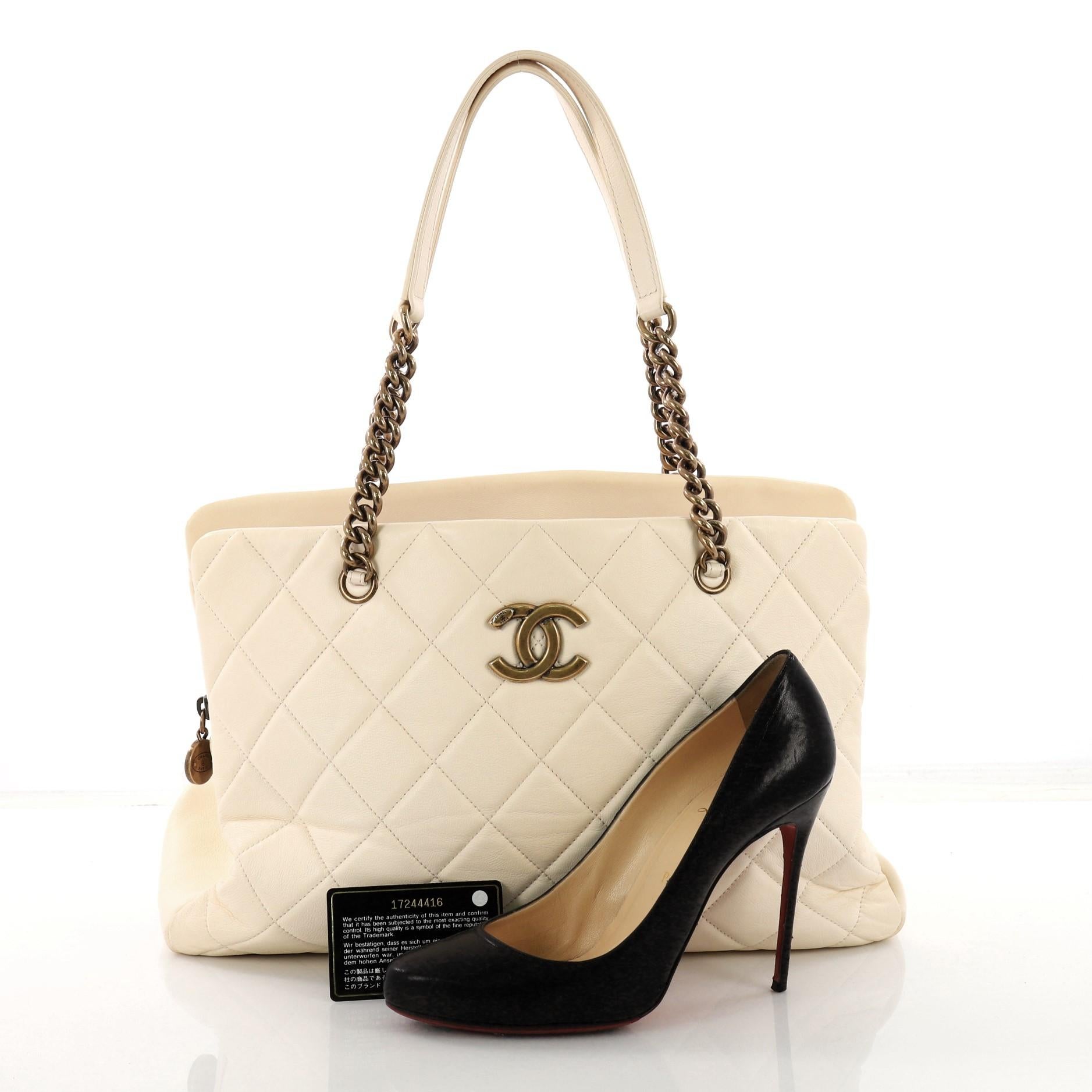 This Chanel CC Crown Tote Quilted Leather Large, crafted in beige quilted leather, features chain straps with leather pads, protective base studs and aged gold-tone hardware. It opens to a beige fabric interior divided into two open compartments and