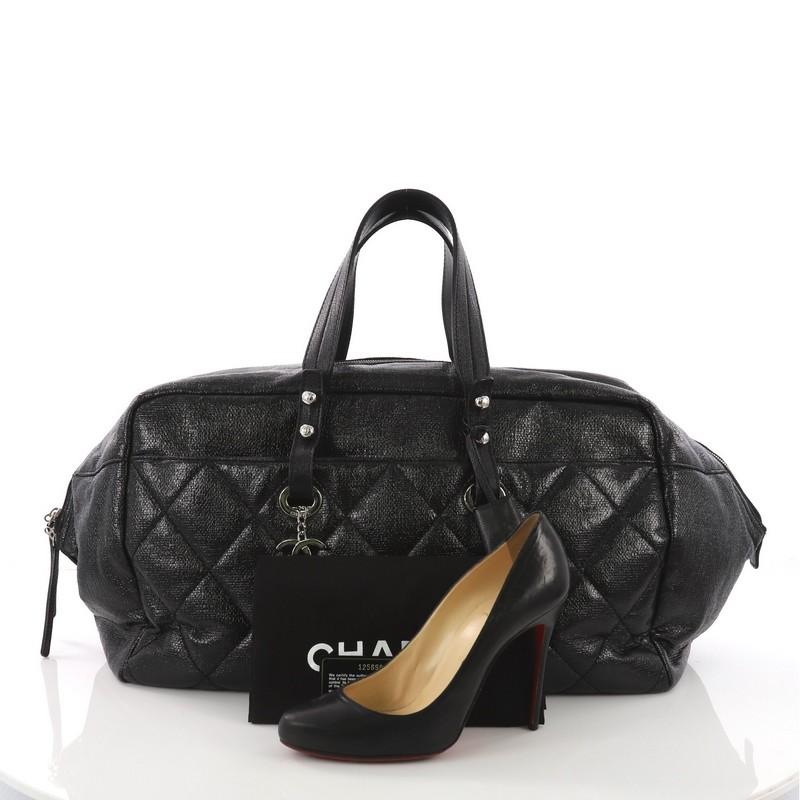 This Chanel Biarritz Satchel Quilted Coated Canvas XL, crafted in black quilted coated canvas, features dual top leather handles, protective base studs, and silver-tone hardware. Its zip closure opens to a black nylon interior with side zip and slip