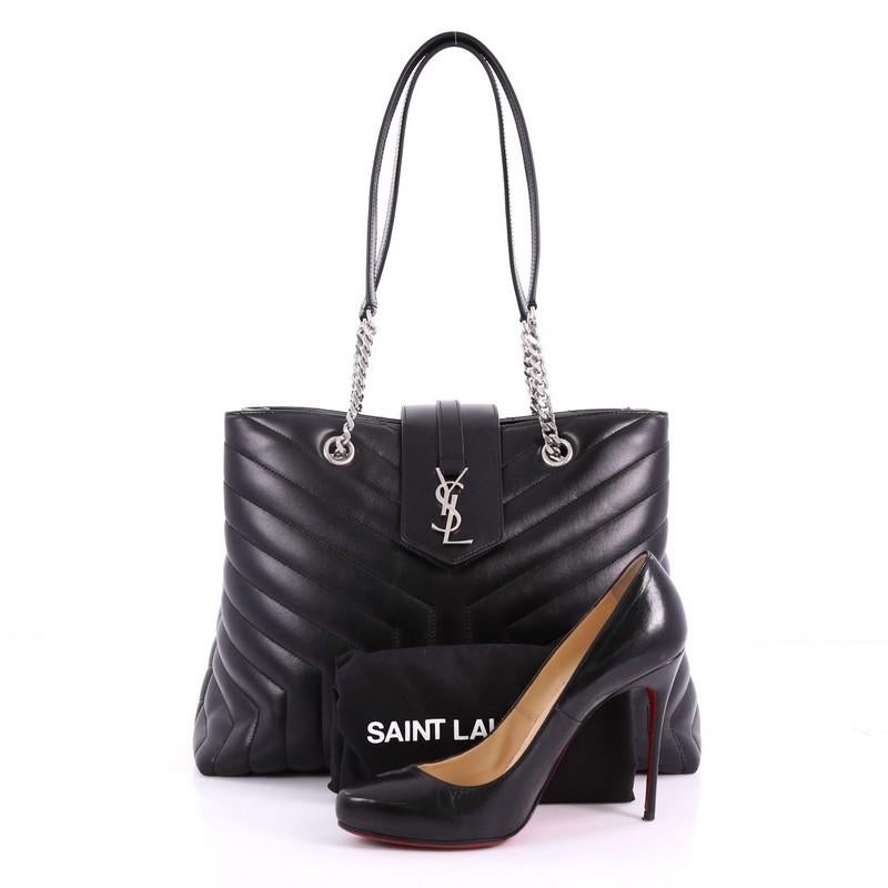 This Saint Laurent LouLou Tote Matelasse Chevron Leather Large, crafted in black chevron matelasse leather, features a dual chain-link strap with shoulder pad, flap tab with YSL metal logo and silver-tone hardware. Its magnetic snap button closure