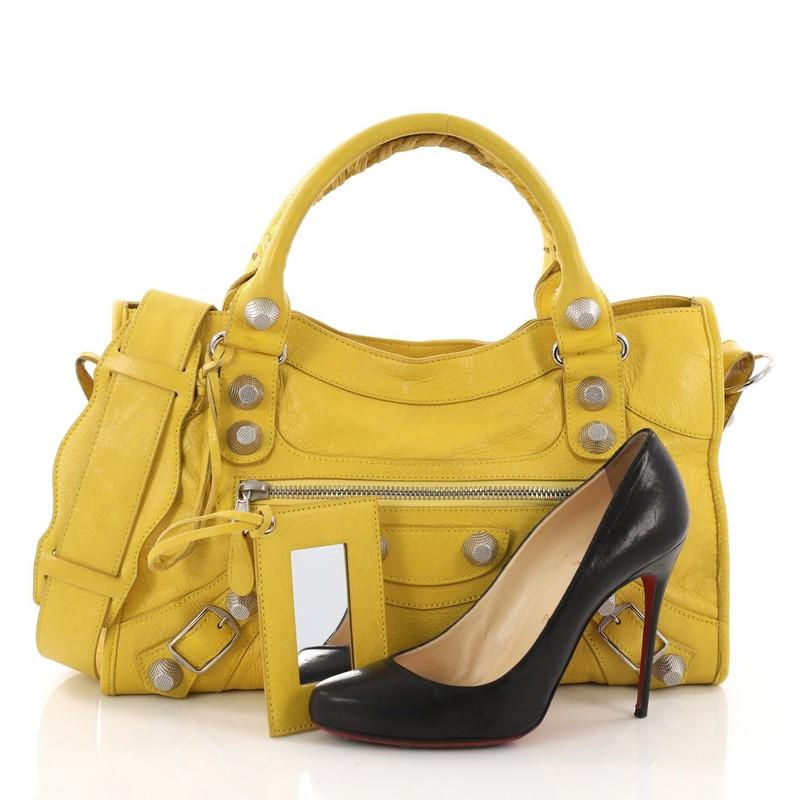 This Balenciaga City Giant Studs Handbag Leather Medium, crafted from yellow leather, features dual braided woven tall handles, exterior front zip pocket, giant studs, and buckle details, and silver-tone hardware. Its top zip closure opens to a