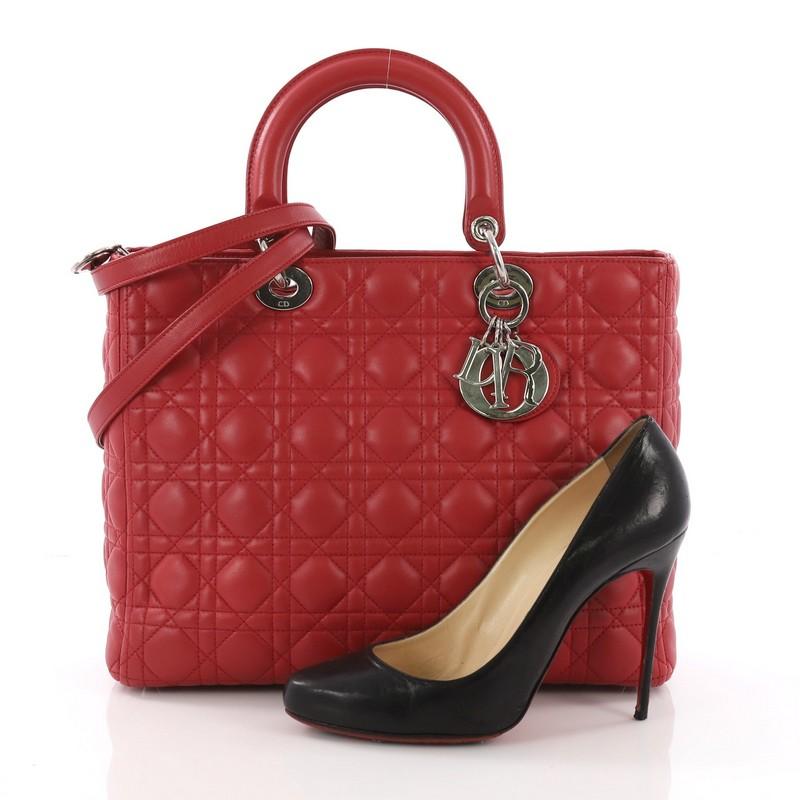 This Christian Dior Lady Dior Handbag Cannage Quilt Lambskin Large, crafted in red cannage quilt lambskin leather, features short dual handles with sleek Dior charms and silver-tone hardware. Its top zip closure opens to a red fabric interior with