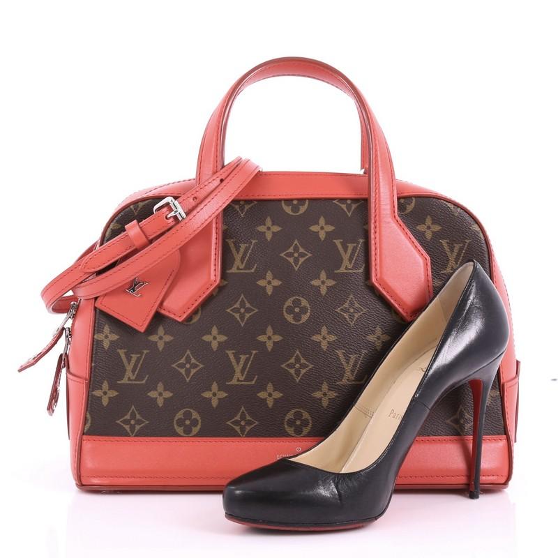 This Louis Vuitton Dora Handbag Monogram Canvas and Calf Leather PM, crafted from brown monogram coated canvas and red calf leather, features dual flat leather top handles, red leather trims and silver-tone hardware. Its two-way zip closure opens to