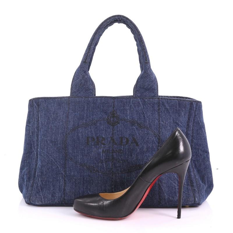 This Prada Canapa Tote Denim Small, crafted in blue denim, features dual handles, side snap buttons, and gold-tone hardware. Its wide top opening showcases a blue denim interior with side zip and slip pockets **Note: Shoe photographed is used as a