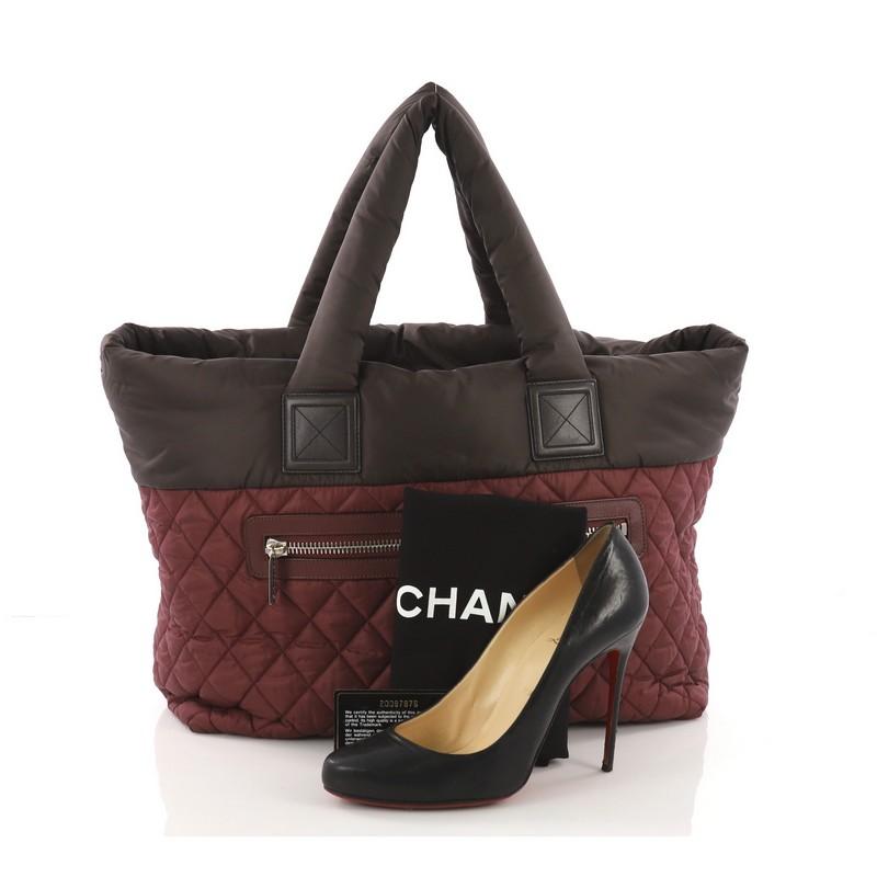 This Chanel Coco Cocoon Reversible Tote Quilted Nylon Medium, crafted from burgundy quilted nylon, features padded top handles, exterior zip pocket, and silver-tone hardware. Its clasp band closure opens to a reversible brown nylon interior with zip