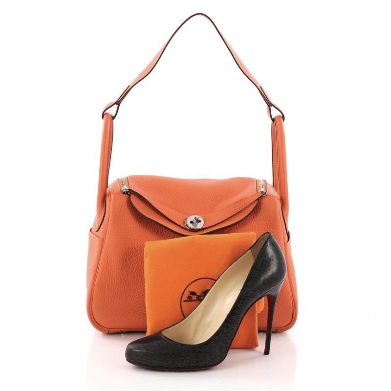 This Hermes Lindy Handbag Clemence 30, crafted from Orange H clemence leather, features dual rolled handles, two side slip pockets, and silver-tone hardware. Its turn-lock and dual zipper closure open to an orange leather interior. Date stamp reads:
