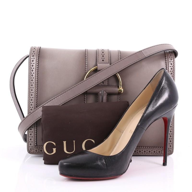 This Gucci Duilio Brogue Shoulder Bag Leather Medium, crafted in taupe leather, features adjustable leather strap and aged gold-tone hardware. Its hook closure opens to a beige canvas interior with middle zip compartment including side zip and slip