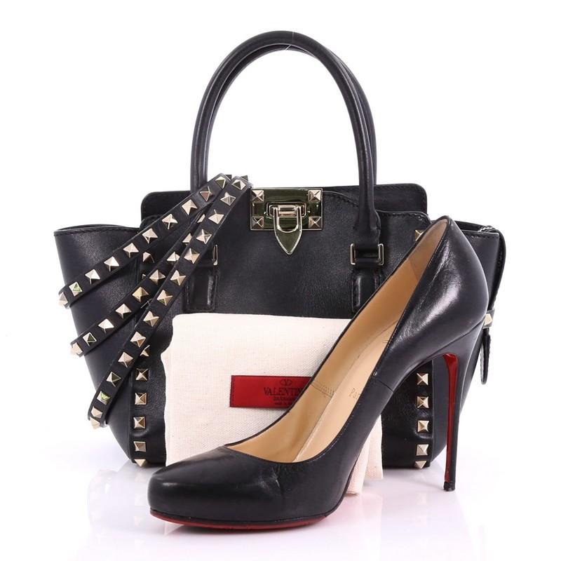 This Valentino Rockstud Tote Rigid Leather Mini, crafted from black leather, features pyramid studded border and strap details, dual rolled handles, and gold-tone hardware. Its flip-clasp and top zip closures open to a black fabric interior with zip