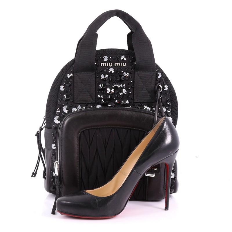 This Miu Miu Backpack Embellished Matelasse Nylon Medium, crafted in black embellished matelasse nylon and black leather, features dual top handles, shoulder strap, exterior front zip pocket, and silver-tone hardware. Its zip closure opens to a