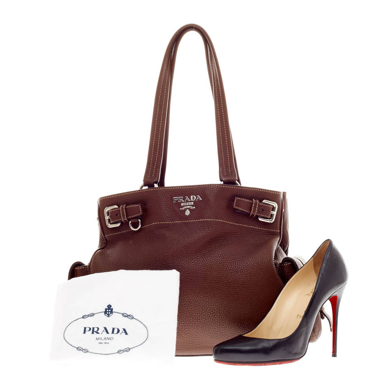 This authentic Prada Side Pocket Vitello Daino Belt Tote is a chic and sturdy everyday bag for both casual or sophisticated looks. Crafted from supple brown pebbled leather, this bag features long shoulder straps, silver-tone hardware, side pockets