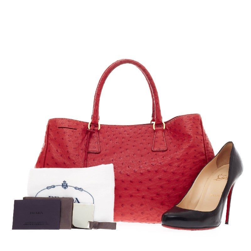 This authentic Prada Struzzo Executive Tote Ostrich Medium is chic and stylish, perfect for any fashionista.  Crafted from genuine textured red ostrich, this elegant bag features dual rolled top handles, a hanging clochette, side triangle Prada logo